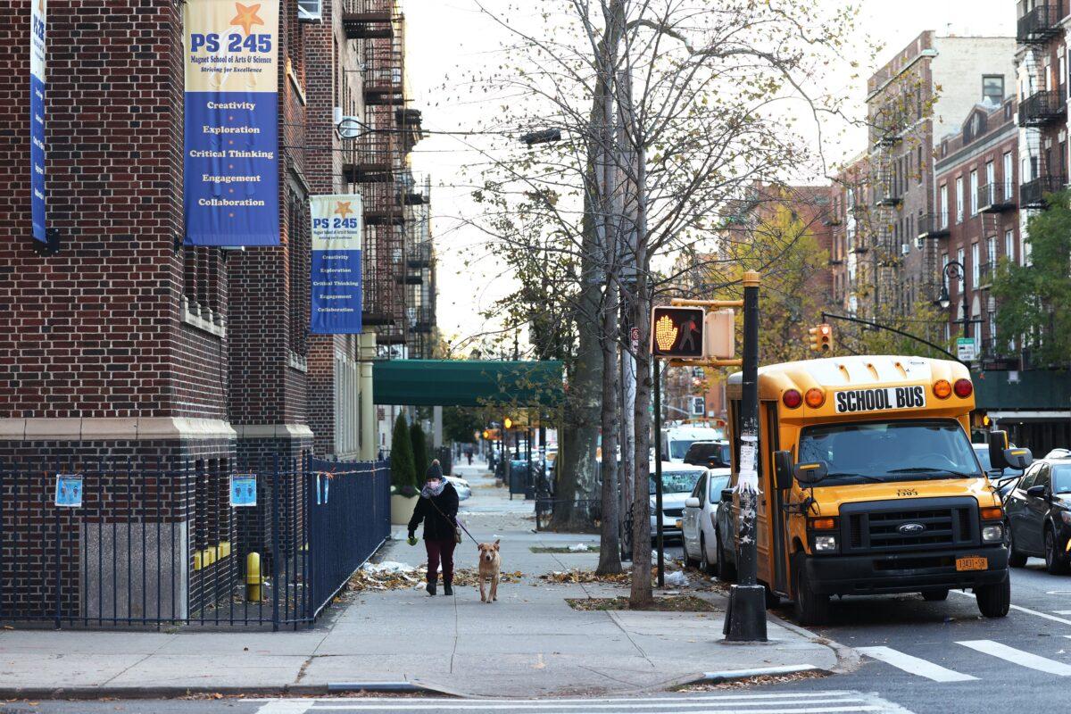 A woman walks her dog past a parked school bus outside of PS 245 in New York City on Nov. 19, 2020. (Michael M. Santiago/Getty Images)