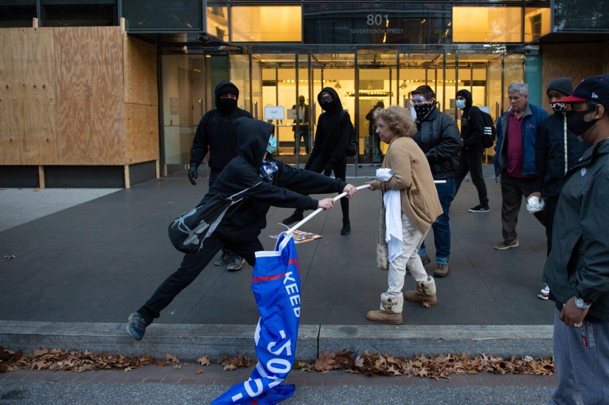 A man dressed in black tries to take a Trump 2020 flag from an elderly supporter of President Donald Trump in Washington on Nov. 14, 2020. (Roberto Schmidt/AFP via Getty Images)