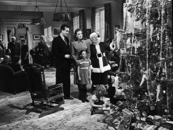 (L–R) Actors John Payne, Maureen O'Hara, Edmund Gwenn (as Santa Claus), and young Natalie Wood stand before a Christmas tree in a still from director George Seaton's 1947 film, “Miracle on 34th Street.” (Hulton Archive/Getty Images)