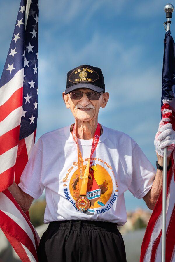 Robert Kohler is a Korean War veteran who includes the American flags in his yearly routine of running the Turkey Trot in Dana Point, Calif., on Nov. 21, 2020. (John Fredricks/The Epoch Times)