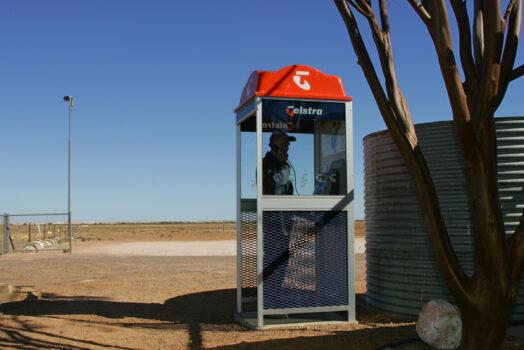 Tim Nagy makes a call from a Telstra public phone booth near the outback opal mining community of Coober Pedy, 05 July 2005. (Torsten Blackwood/AFP via Getty Images)