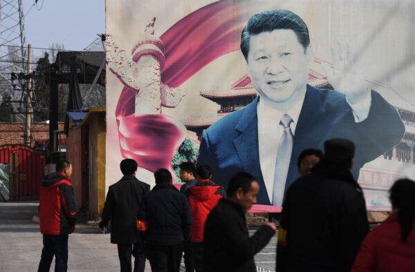 People stand near a faded propaganda billboard featuring an image of Chinese leader Xi Jinping in a car park in Beijing on March 19, 2018. (Greg Baker/AFP via Getty Images)