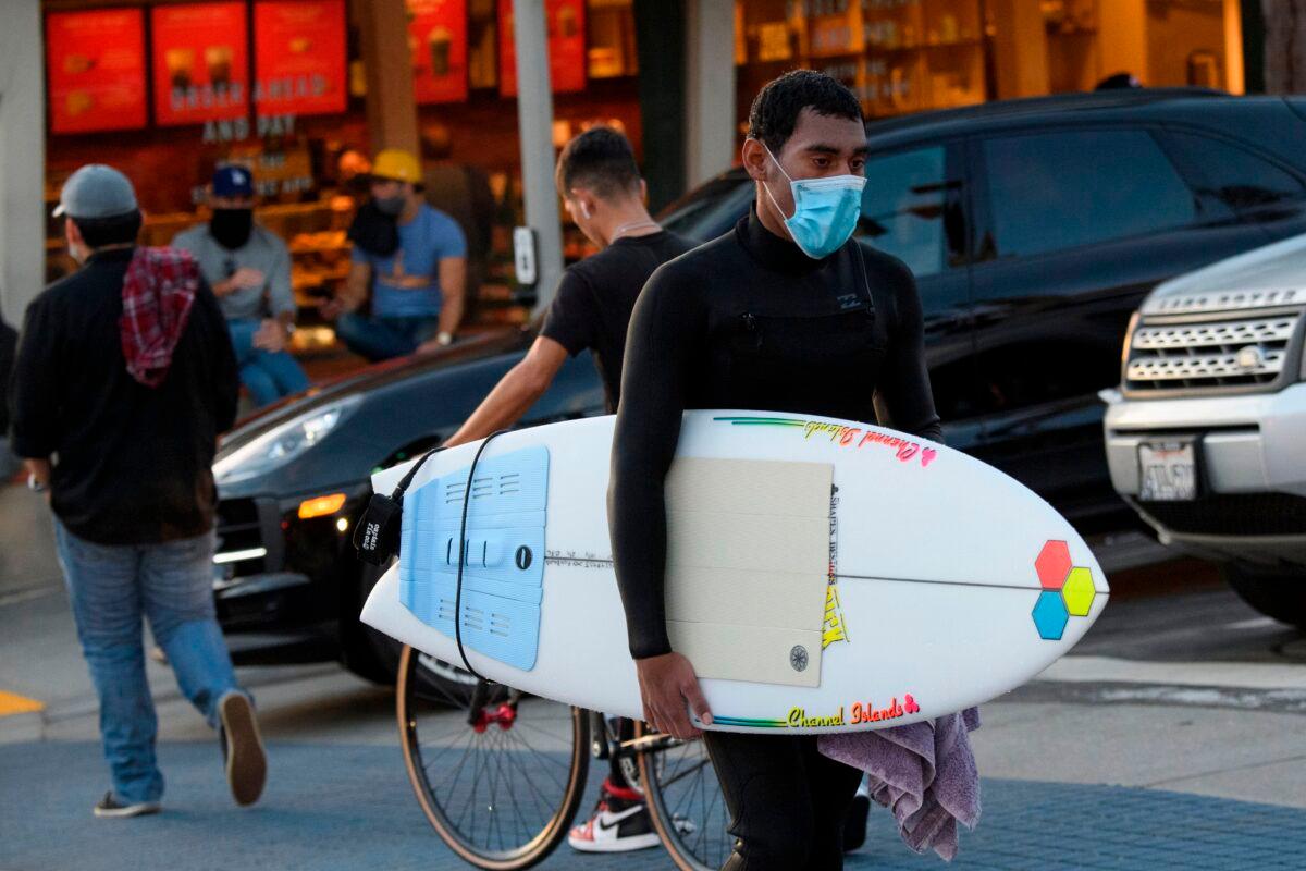 A surfer wearing a face mask carries his surfboard in Manhattan Beach, Calif., on Nov. 21, 2020. (Patrick T. Fallon/AFP via Getty Images)