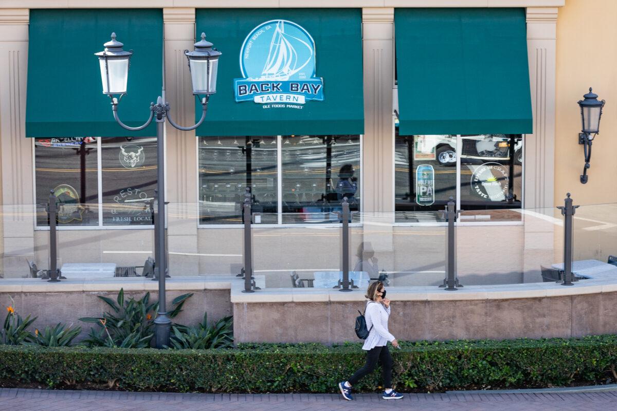 A woman walks during the near-statewide lockdown past the empty patio area of The Back Bay Tavern in Newport Beach, Calif., on Dec. 9, 2020. (John Fredricks/The Epoch Times)
