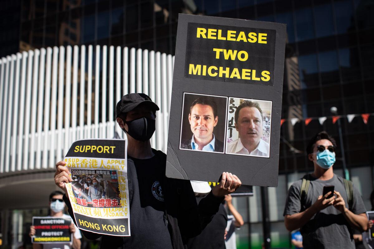 A person holds a sign with photographs of Michael Kovrig and Michael Spavor, who have been detained in China since December 2018, as people gather for a rally in support of Hong Kong democracy, in Vancouver, B.C., on Aug. 16, 2020. (Darryl Dyck/The Canadian Press)