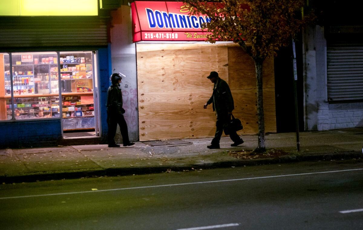 A man and police officer walk past a shuttered store after looting during a citywide curfew in Philadelphia, Penn., on Oct. 28, 2020. (Mark Makela/Getty Images)