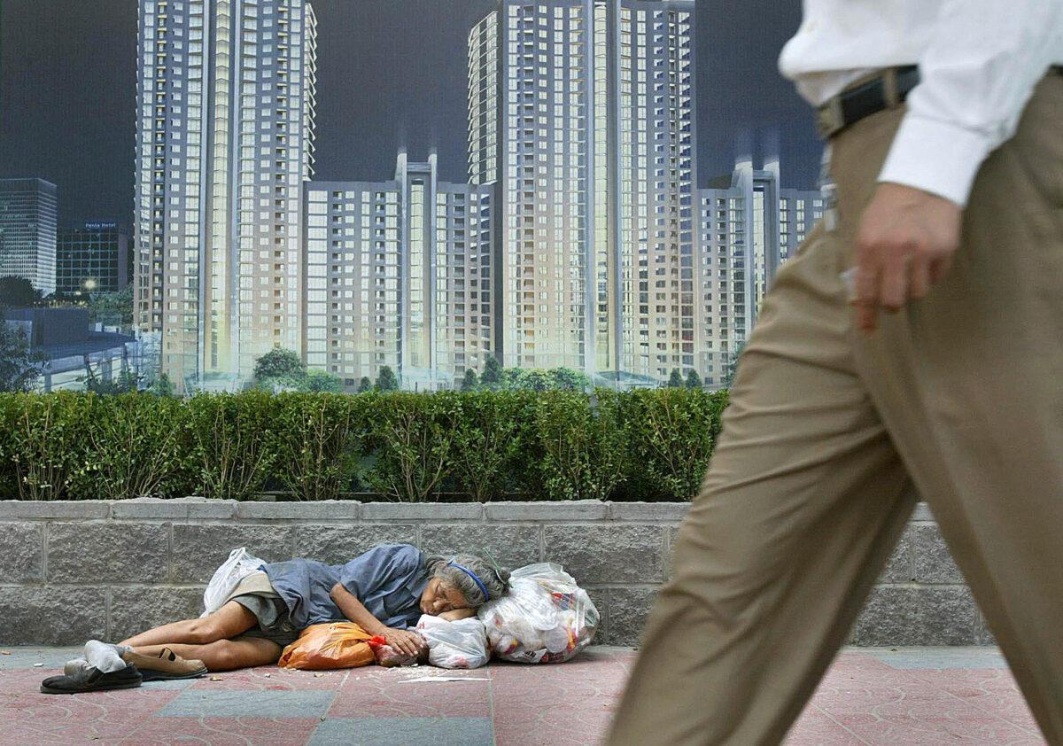 A homeless woman sleeps beneath an advertising billboard promoting new urban development in Beijing on Aug. 21, 2003. (Frederic J. Brown/AFP via Getty Images)