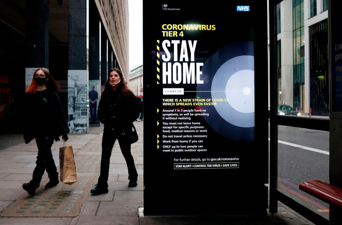 People, some wearing masks, walk past a bus stop with a government message about the CCP virus tier 4 restrictions urging people to stay home in London on Dec. 29, 2020. (Tolga Akmen/AFP via Getty Images)