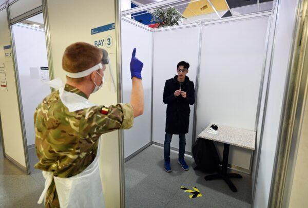 A soldier assists a member of the public as they take a COVID-19 test in a booth before passing it to soldiers for processing at a testing centre set up in St John's Market in Liverpool, northwest England on Nov. 11, 2020, during a city-wide mass testing pilot operation. (Paul Ellis/AFP via Getty Images)