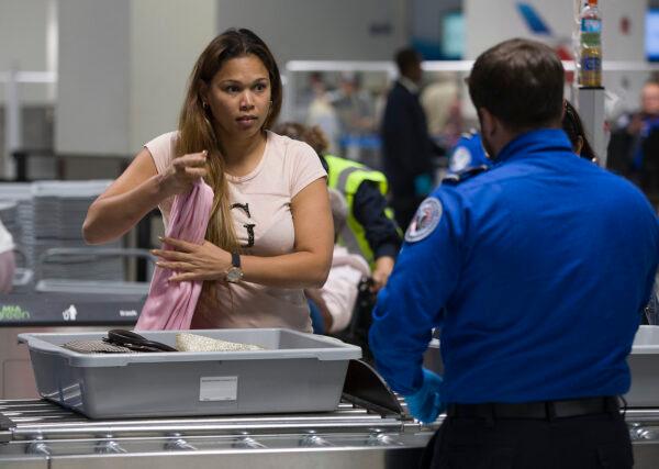 A traveler places her carry on items into a tray as a Transportation Security Administration (TSA) agent helps her use the 3D scanner at the Miami International Airport on May 21, 2019. (Joe Raedle/Getty Images)