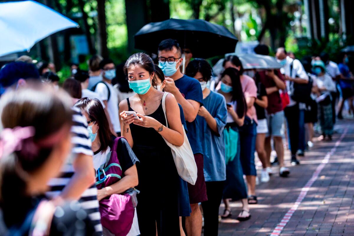 A woman (center L) uses her phone while waiting to vote during primary elections in Hong Kong on July 12, 2020. (Issac Lawrence/AFP via Getty Images)