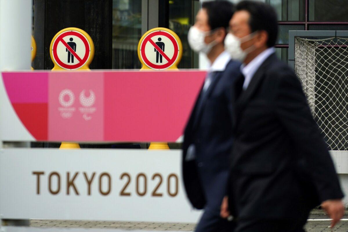 People wearing protective masks to help curb the spread of the coronavirus walk near a banner of Tokyo 2020 Olympics and Paralympic games in Tokyo Friday, Jan. 15, 2021. (Eugene Hoshiko/AP Photo)