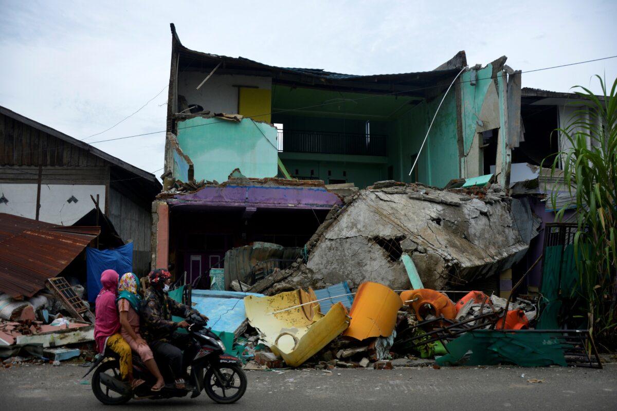 Locals ride a motorbike past a collapsed house following an earthquake in Mamuju, West Sulawesi province, Indonesia, on Jan. 17, 2021. (Abriawan Abhe/Antara Foto via Reuters)