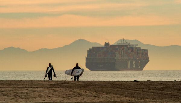 Surfers walk on the beach as a cargo ship waits in the bay in Los Angeles, Calif., on Jan. 12, 2021. (John Fredricks/The Epoch Times)