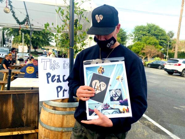 Artist Ponti Lambros holds pictures of a symbol he created—he has been spreading it in sticker form in Los Angeles to signify support of local businesses—outside the Pineapple Hill Saloon & Grill on Jan. 7, 2021. (Jamie Joseph/The Epoch Times)