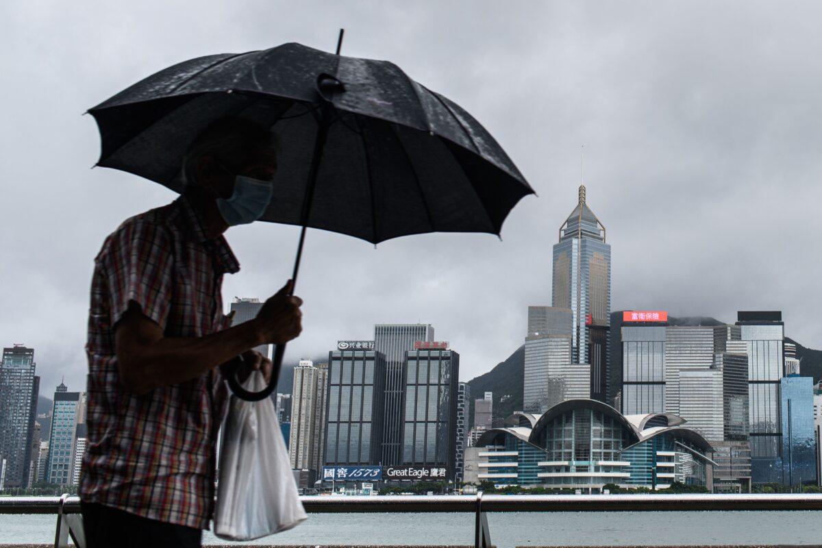 A man uses his umbrella on Kowloon's Tsim Sha Tsui waterfront that faces Victoria Harbor and the Hong Kong Island skyline (back) in Hong Kong on Aug. 19, 2020. (Anthony Wallace/AFP via Getty Images)