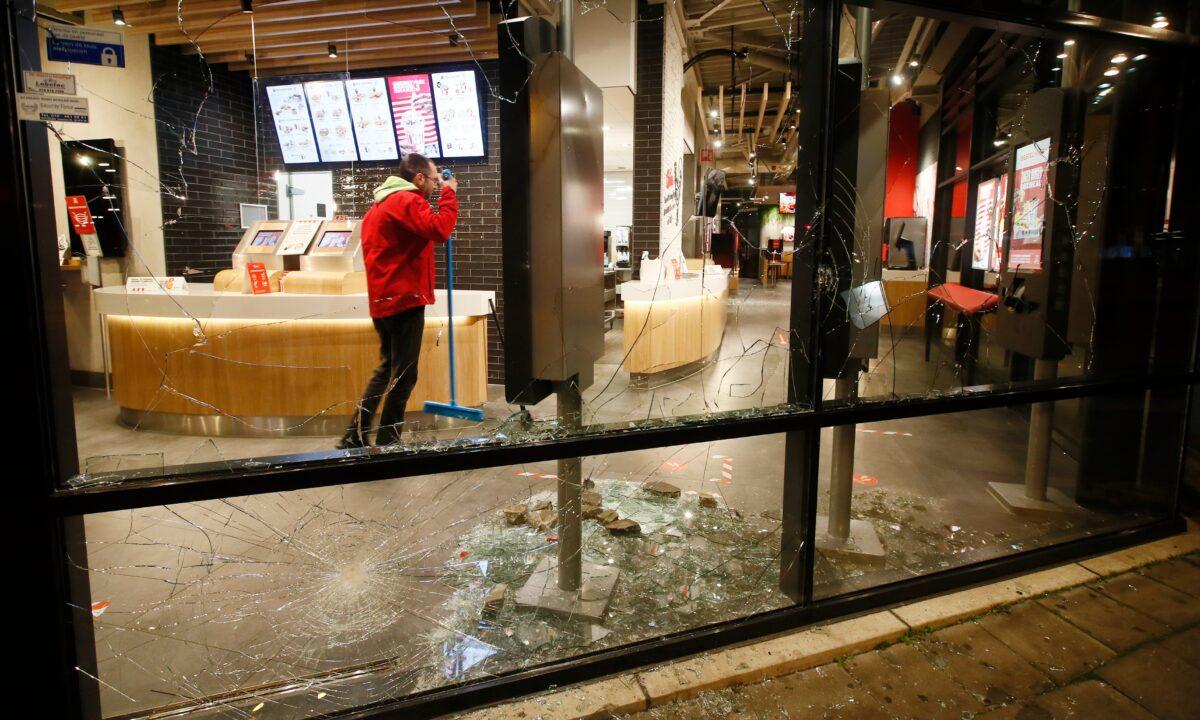 A man cleans up broken glass from the smashed windows in a fast-food restaurant that was damaged in protests against a nation-wide curfew in Rotterdam, Netherlands, on Jan. 25, 2021. (Peter Dejong/AP Photo)