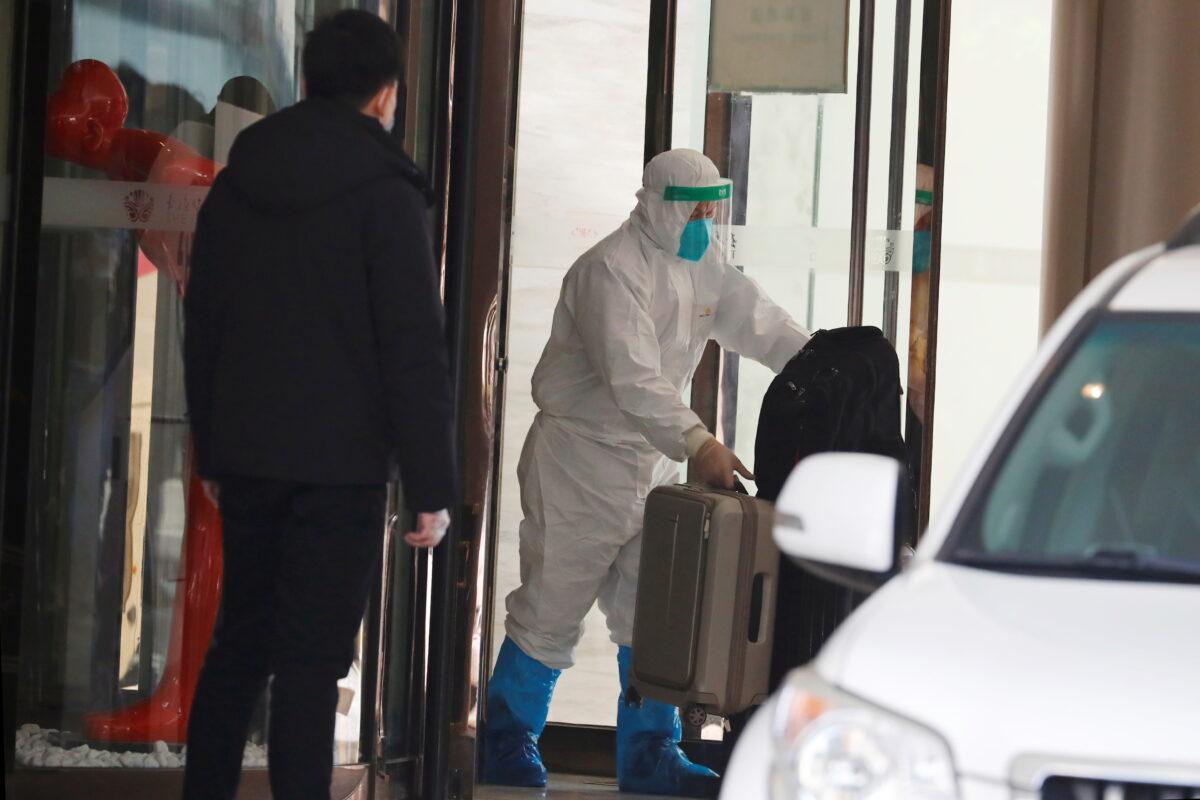A staff member in protective gear moves luggage before members of the World Health Organisation (WHO) team tasked with investigating the origins of the coronavirus disease (COVID-19) pandemic leave their quarantine hotel in Wuhan, Hubei province, China Jan. 28, 2021. (REUTERS/Thomas Peter)