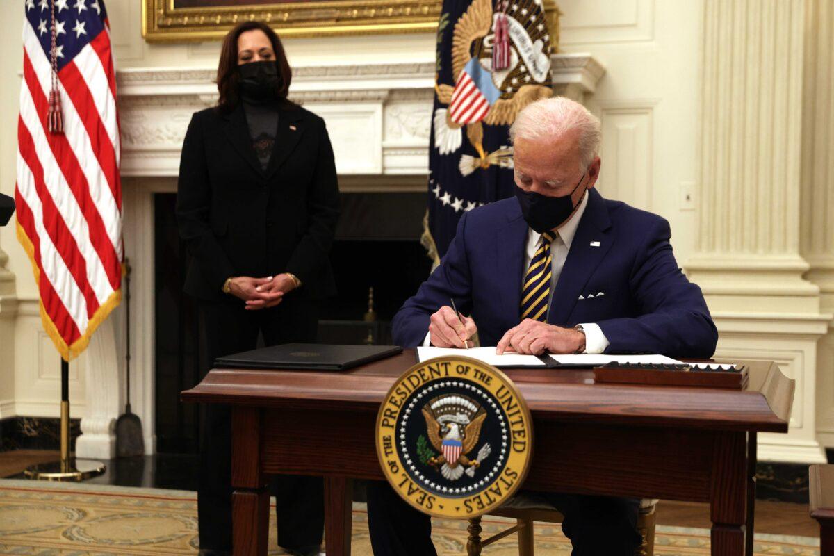 President Joe Biden signs an executive order as Vice President Kamala Harris looks on during an event on economic crisis in the State Dining Room of the White House in Washington on Jan. 22, 2021. (Alex Wong/Getty Images)