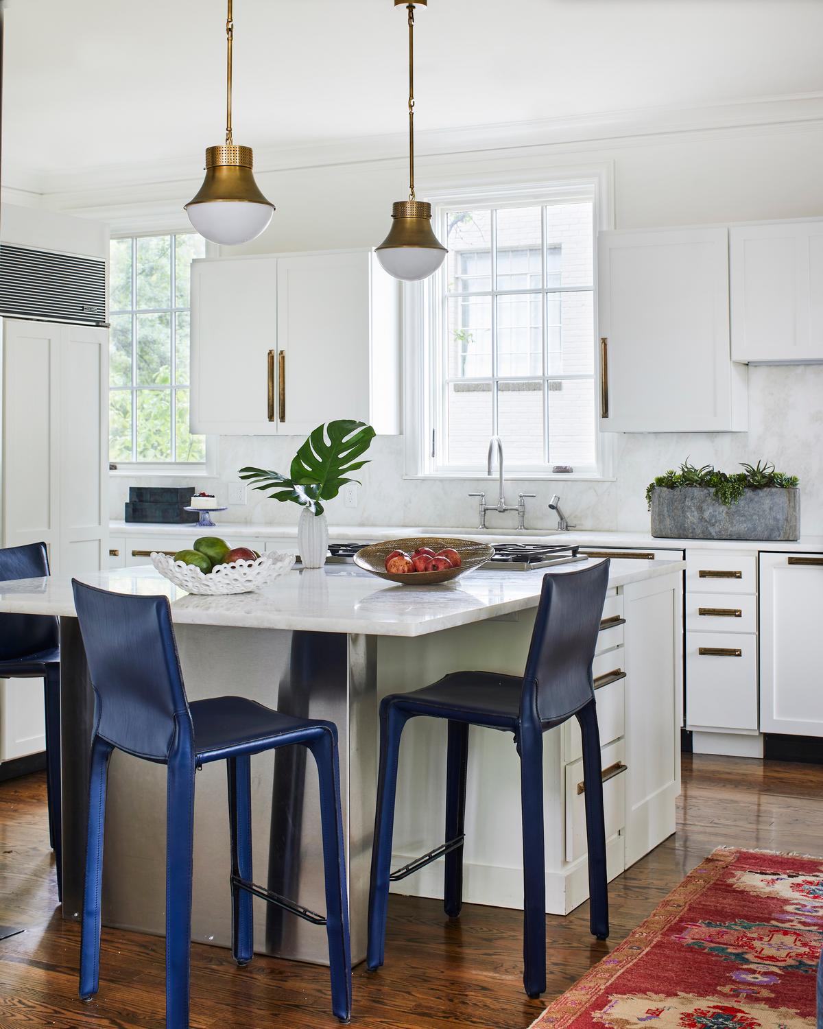 In the kitchen, new lighting, countertops, and cabinet hardware were installed to maximize functionality. A new marble countertop adds elegance, complementing the brass hardware while contrasting with the sapphire-blue bar stools. (Laurey Glenn)
