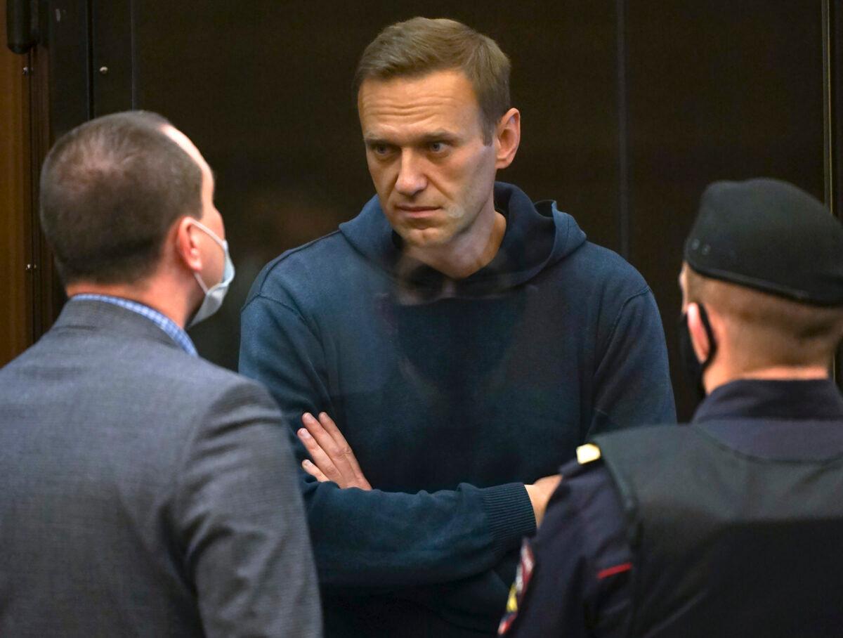 Russian opposition leader Alexei Navalny talks to one of his lawyers, left, while standing in the cage during a hearing to a motion from the Russian prison service to convert the suspended sentence of Navalny from the 2014 criminal conviction into a real prison term in the Moscow City Court in Moscow, Russia, on Feb. 2, 2021. (Moscow City Court via AP)