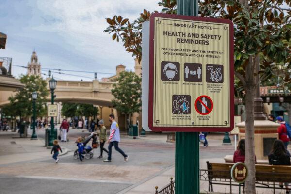 A family walks by a coronavirus saftey sign at Disneyland California Adventure themepark in Anaheim, Calif., on Feb. 1, 2021. (John Fredricks/The Epoch Times)
