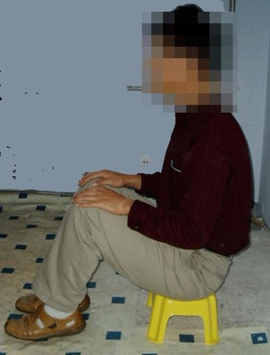 A reenactment of sitting on a small stool, a method often used in Chinese prisons to torture Falun Gong practitioners who refuse to give up on their faith. (<a href="https://en.minghui.org/">Minghui.org</a>)