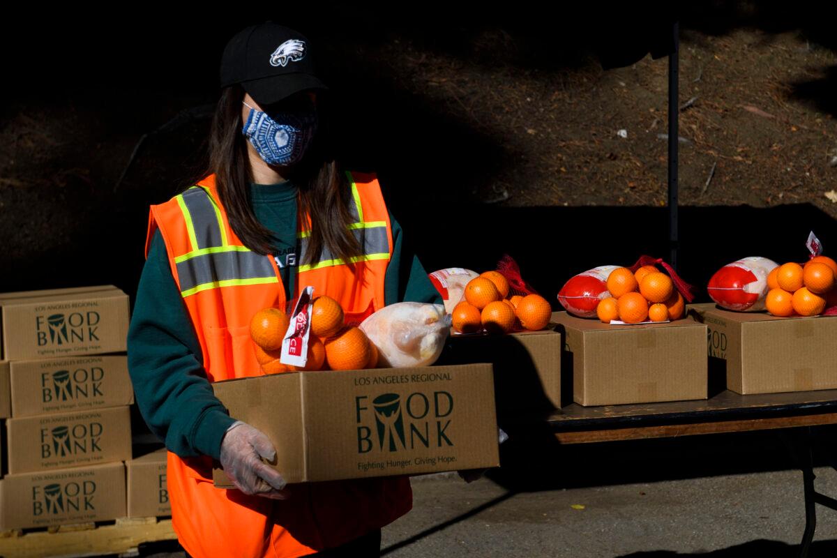A worker carries a box of groceries to load into a vehicle at a mobile food distribution from the Los Angeles Regional Food Bank at the Hollywood Bowl during the CCP virus pandemic in Los Angeles, on Feb. 5, 2021. (Patrick T. Fallon/AFP via Getty Images)