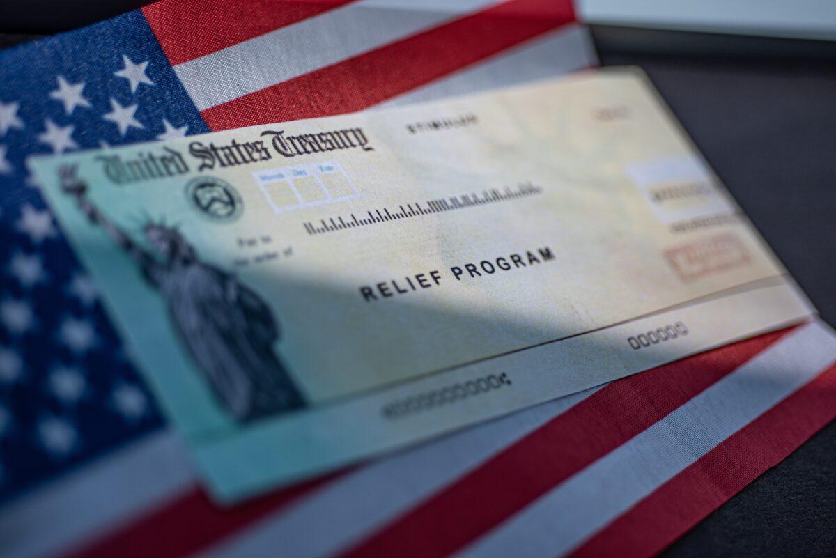 COVID-19 economic Stimulus check on blurred USA flag and sun light background. Relief program concept. (Shutterstock)