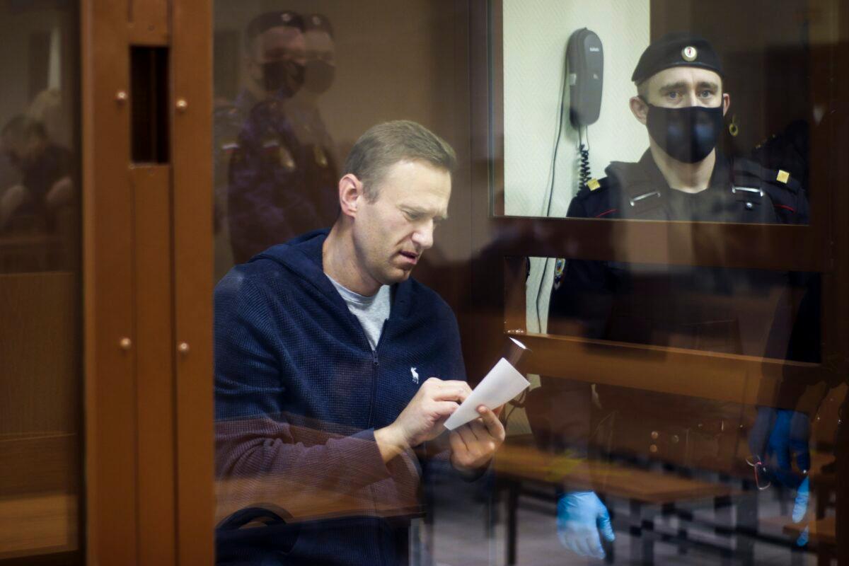 Russian opposition leader Alexei Navalny writes a note in a cage during a hearing on charges of defamation in the Babuskinsky District Court in Moscow, Russia., on Feb. 12, 2021. (Babuskinsky District Court Press Service via AP)