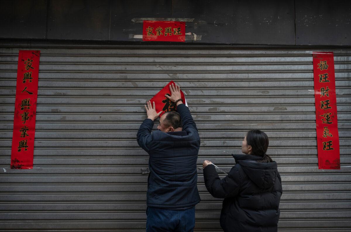 A shopkeeper puts up the character "Fu" for good luck outside his shop before opening for the Chinese New Year marking the Year of the Ox, and Spring Festival in a commercial area in Beijing, China, on Feb. 11, 2021. (Photo by Kevin Frayer/Getty Images)