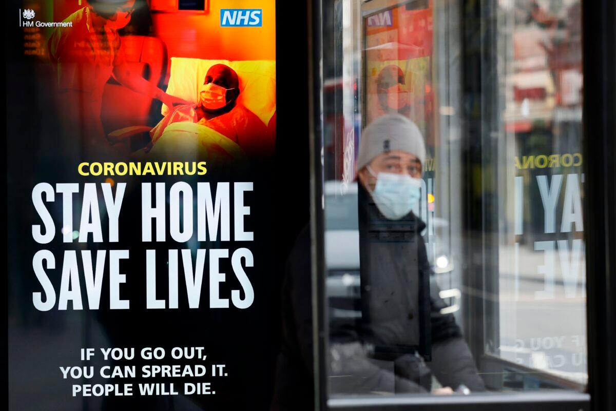 A commuter wears a face mask as he sits in a bus shelter with NHS signage promoting "Stay Home, Save Lives" in Chinatown, central London, on Jan. 8, 2021. (Tolga Akmen /AFP via Getty Images)