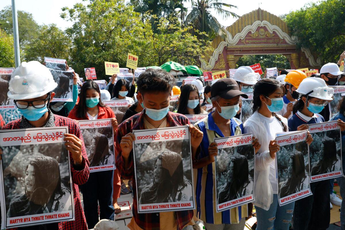 Mandalay University graduates bow their heads as they hold posters with an image of Mya Mya Thwate Thwate Khaing, the 19-year old woman shot by police in Naypyitaw, on Feb. 9, during an anti-coup protest in Mandalay, Burma, on Feb. 14, 2021. (AP Photo)