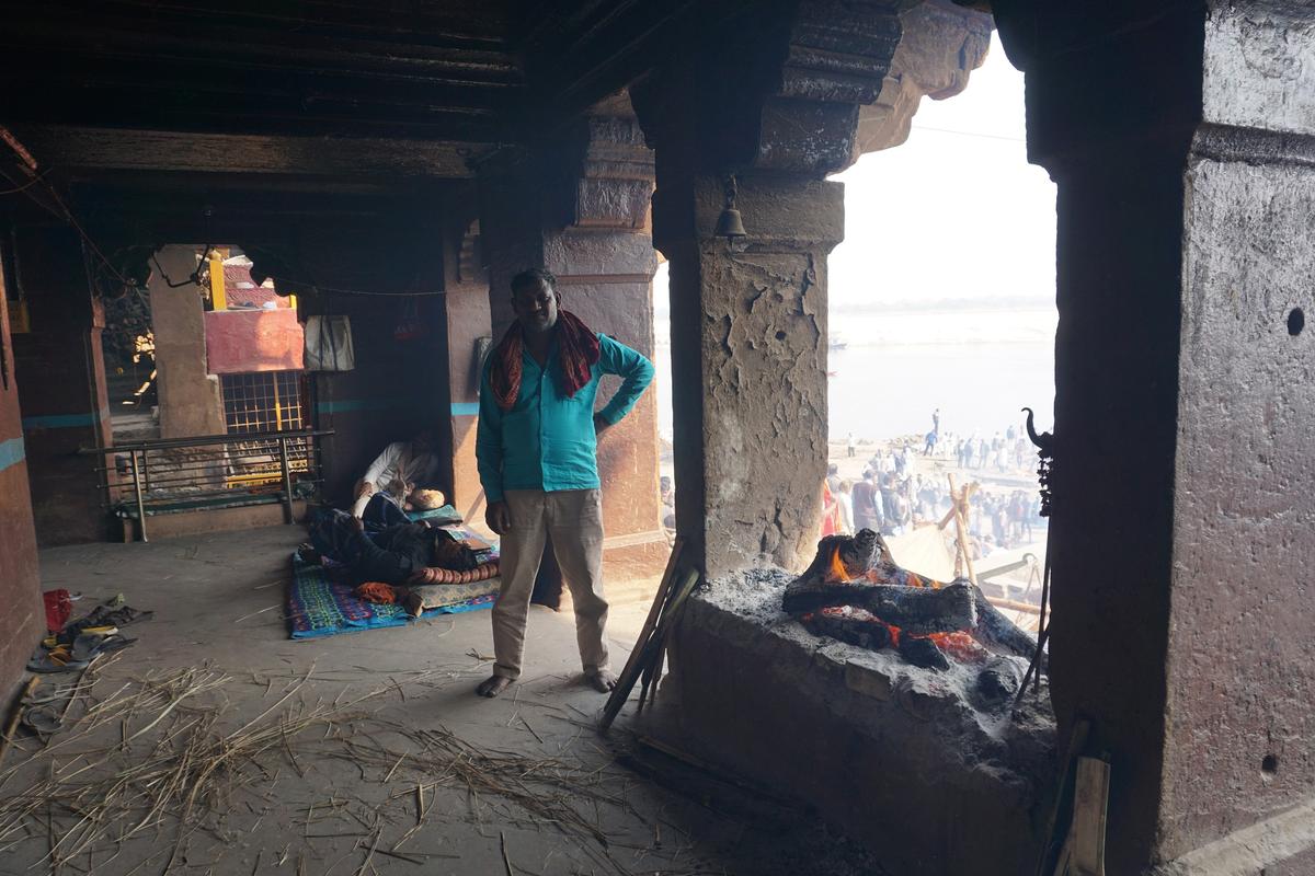 Rajesh Chaudhary stands near the dhuni, or sacred fire, that lends fire to every pyre at the ancient Manikarnika ghat in Kashi on Feb. 12, 2021. (Venus Upadhayaya/Epoch Times)