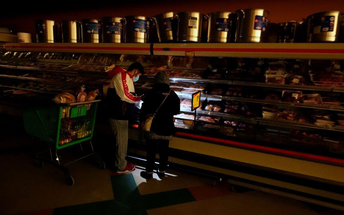 Customers use the light from a cell phone to look in the meat section of a grocery store in Dallas, Texas, on Feb. 16, 2021. (LM Otero/AP Photo)