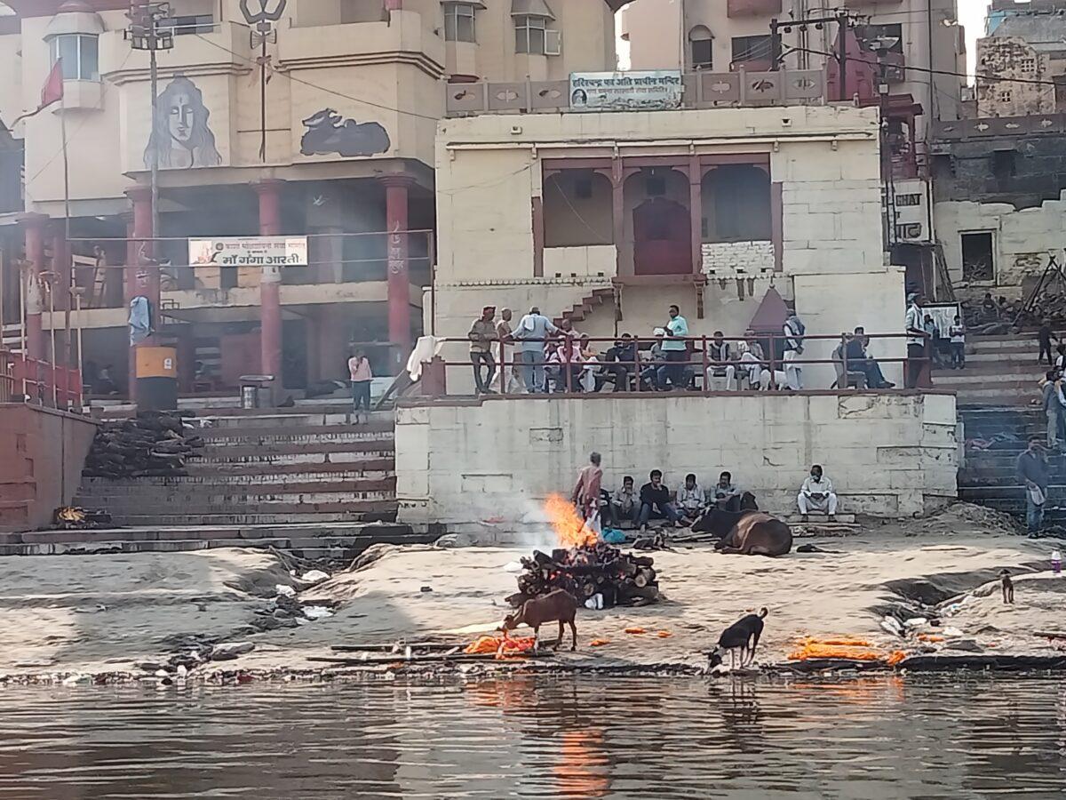 A pyre burns on the Harish Chandra ghat (bank) of the Ganges in the ancient city of Kashi on Feb. 18, 2021, while mourners watch. (Venus Upadhayaya/Epoch Times)