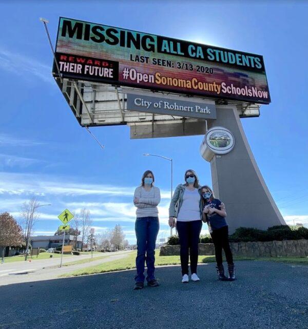 (L–R) Mary Lockler, Andrea Pedersen, and Olivia Soderling stand under the electronic billboard next to Highway 101 in Rohnert Park, Calif., on Feb. 25, 2021. (Ted Lin/The Epoch Times)