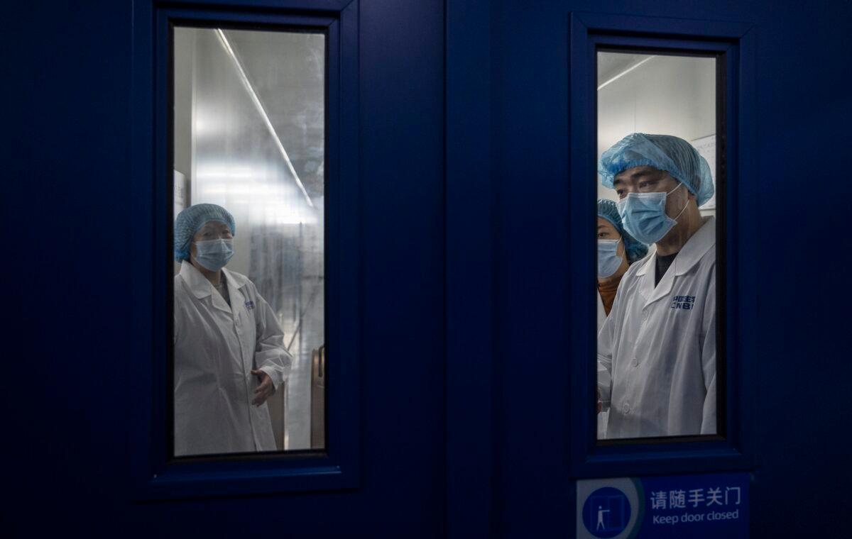 Workers wait to open the secure door in the packaging area of Sinopharm CNBG's inactivated SARS-Cov-2 vaccine for COVID-19 during a media tour organized by the State Council Information Office in Beijing, China on Feb. 26, 2021. (Kevin Frayer/Getty Images)