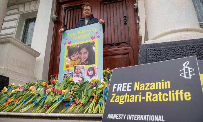 Richard Ratcliffe, the husband of British charity worker Nazanin Zaghari-Ratcliffe, who is being held in Iran poses for a photo with a giant Mother's Day card and flowers left on the steps of the Iranian Embassy, in Knightsbridge, London. (Dominic Lipinski/PA via AP)