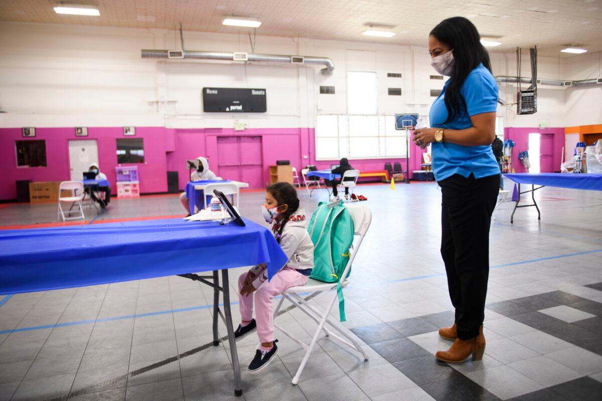 A YMCA staff member assists a child as they attend online classes at a learning hub inside the Crenshaw Family YMCA, as schools remain closed to in-person instruction, in Los Angeles, Calif., on Feb. 17, 2021. (Patrick T. Fallon/AFP via Getty Images)