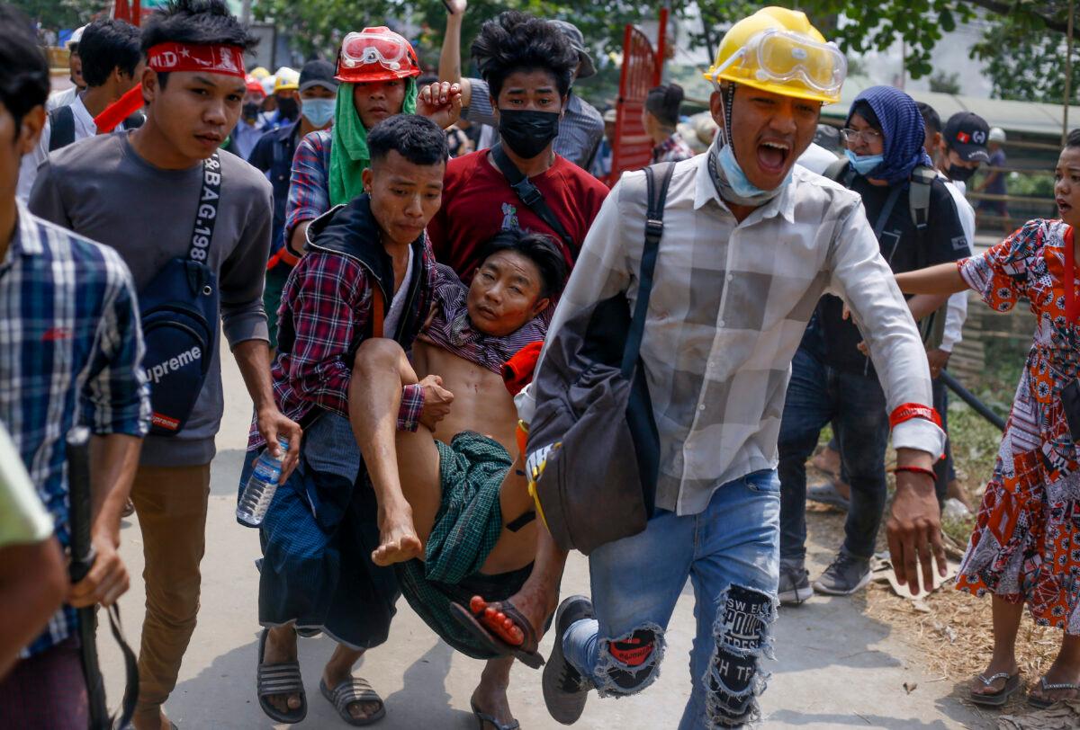 Anti-coup protesters carry an injured man following clashes with security in Yangon, Burma, on March 14, 2021. (AP Photo)