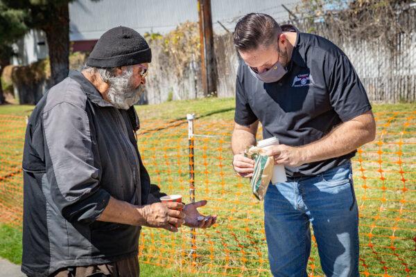 Charity on Wheels Managing Director Zach Southall gives coffee to a homeless man in Orange, Calif., on March 5, 2021. (John Fredricks/The Epoch Times)