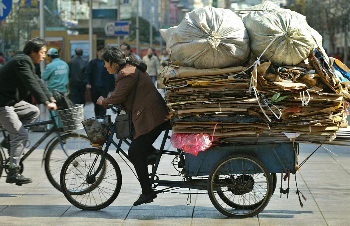A migrant worker rides a tricycle full of waste along a street in Shanghai, China on Feb. 18, 2003. (Liu Jin/AFP via Getty Images)