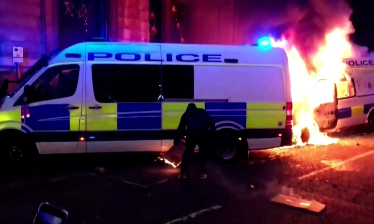 In this still image from a video, a man is seen trying to set a police van on fire in Bristol, England, on March 21, 2021. (Reuters/Screenshot via The Epoch Times)