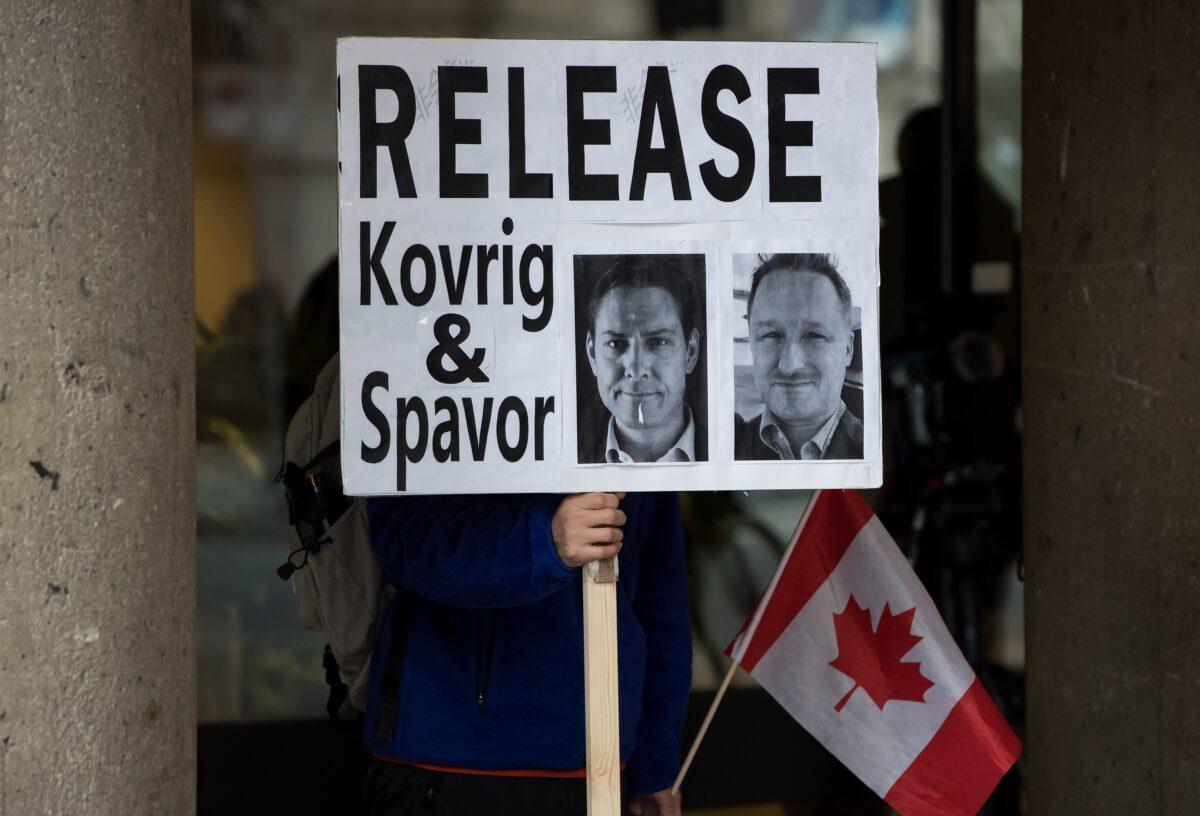 A young man holds a sign bearing photographs of Michael Kovrig and Michael Spavor, who have been detained in China for more than a year, outside the B.C. Supreme Court, where Huawei Chief Financial Officer Meng Wanzhou attends a hearing in Vancouver on Jan. 21, 2020. (Darryl Dyck/The Canadian Press)