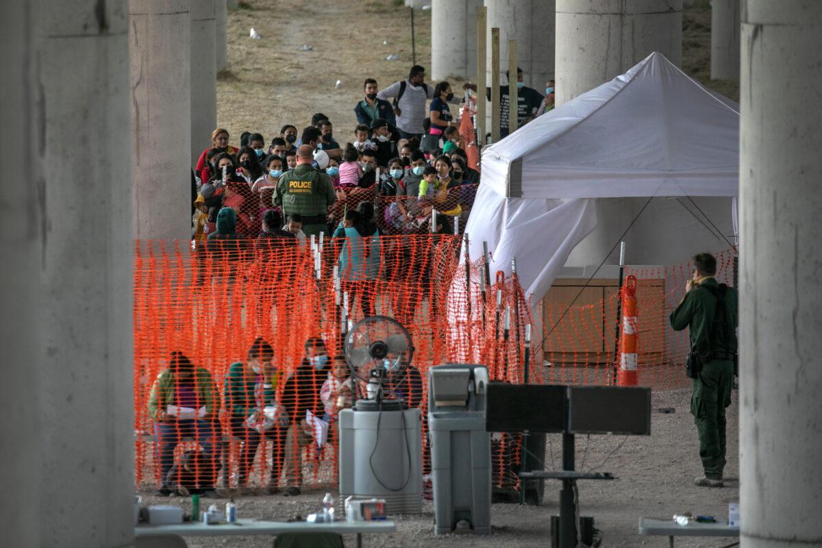 Illegal immigrants listen to instructions at an outdoor Border Patrol processing center under the Anzalduas International Bridge after crossing the Rio Grande from Mexico near Mission, Texas, on March 23, 2021. (John Moore/Getty Images)