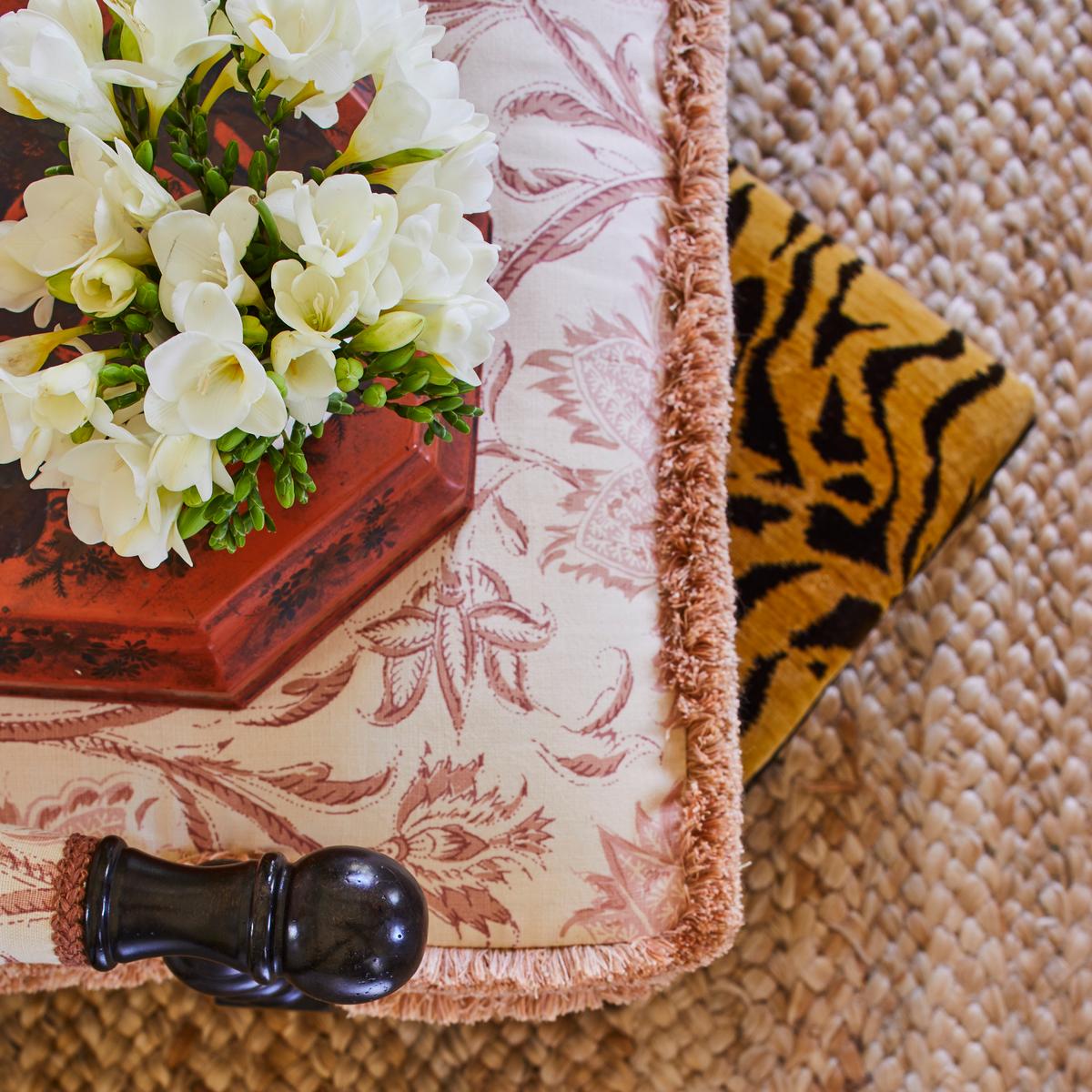 Unexpected pairings of patterns bring delight and offset expectations. Here, two-toned floral upholstery with whimsical seams plays host to a tiger print footstool. (Laurey Glenn)