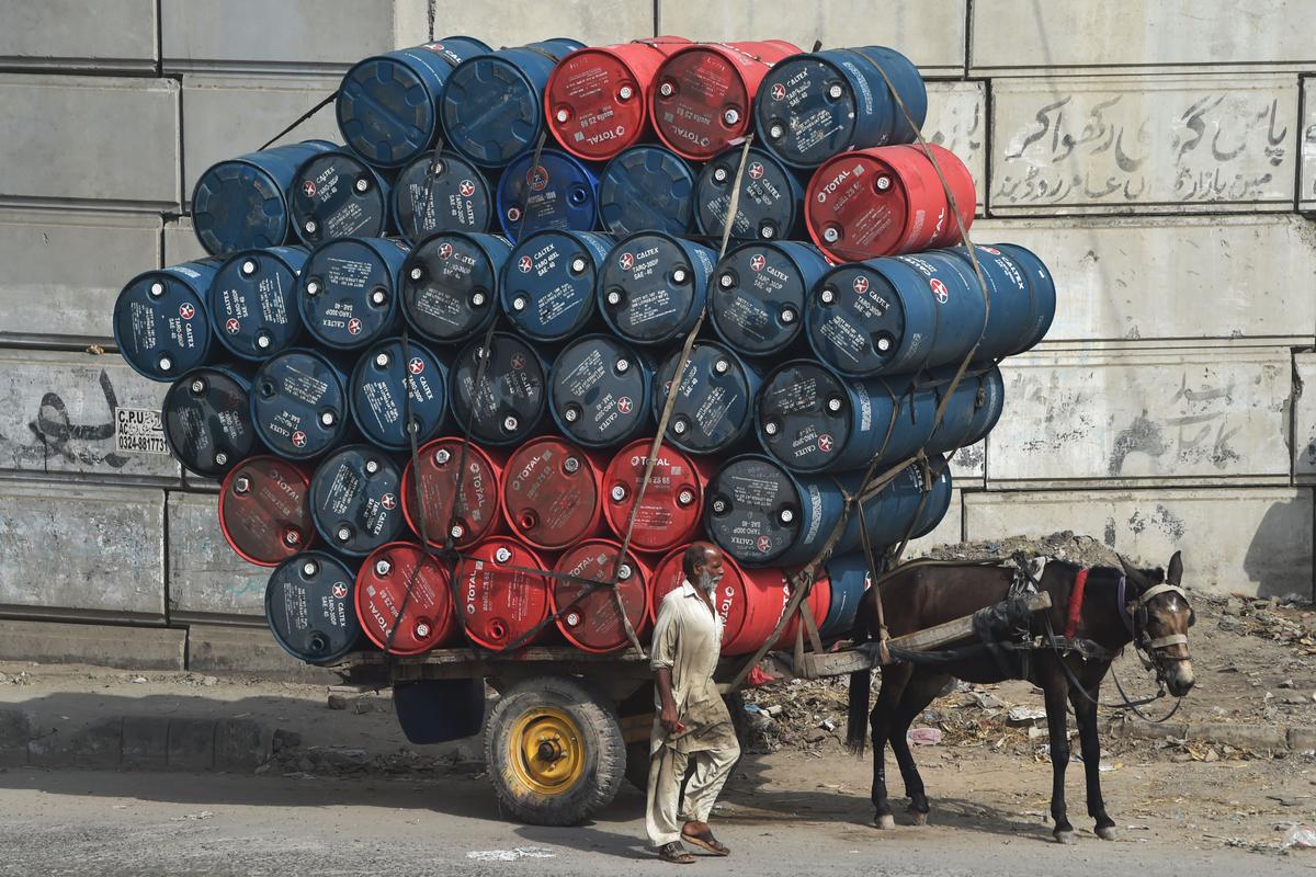A man stands next to a horsecart laden with oil drums on a street in Lahore, Pakistan, on Sept. 27, 2020. (Arif Ali/AFP via Getty Images)