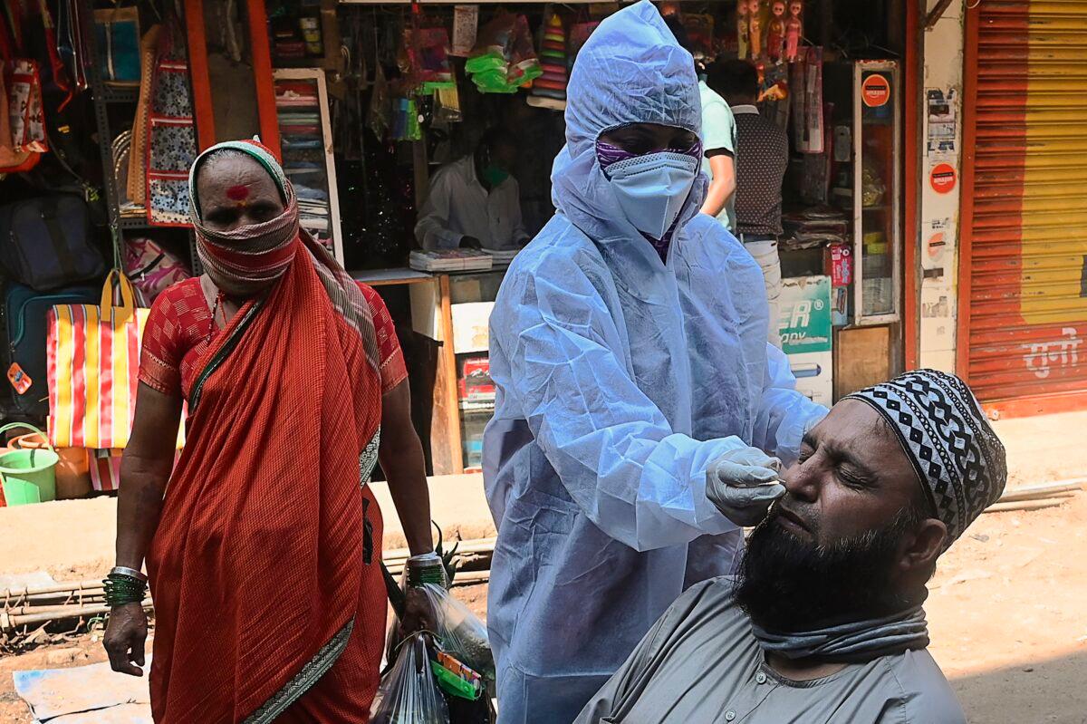 A health worker (C) takes a nasal swab of a resident as an elderly looks on during a COVID-19 RT PCR and Rapid Antigen test, at a market in Mumbai, India, on Nov. 23, 2020. (Indranil Mukherjee/AFP via Getty Images)