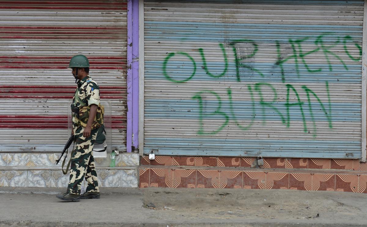 An Indian paramilitary trooper stands guard in Srinagar alongside graffiti bearing the name of the slain Hizbul Mujahideen commander Burhan Wani during a curfew continued across large parts of Indian-administered Kashmir weeks after his death, on July 31, 2016. (TAUSEEF MUSTAFA/AFP via Getty Images)